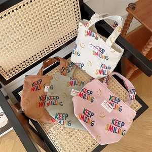 Detail of corduroy tote bags in multiple colors with Keep Smiling print and woven labels