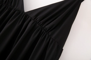 Détail d'une robe midi noire avec col en V, tissu plissé élégant et légers reflets brillants