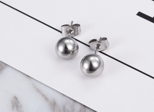 Close-up of polished silver ball stud earrings with butterfly backs on a marble surface
