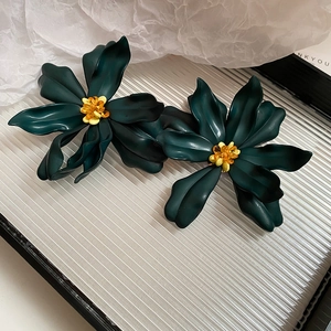 Close-up of matte dark green acrylic flower earrings with yellow and orange bead centers