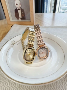 Detail view of gold and rose gold oval quartz watches on a decorative white plate