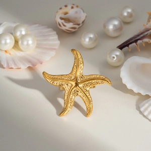 Bague étoile de mer dorée avec texture métallique sur fond marin avec perles et coquillages