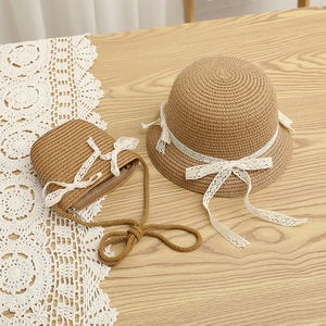 Detailed view of straw hat and matching crossbody bag with white lace bow on wood