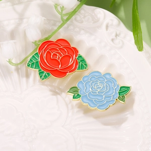 Exquisite colorful floral enamel brooches in red and blue on a white ceramic plate