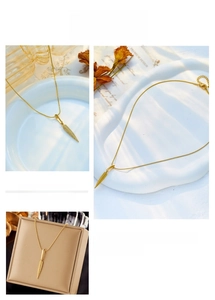 Dettaglio macro della collana con ciondolo a piuma dorata con trama metallica e design
