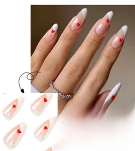 Macro detail of almond-shaped French nails with white tips and tiny red heart accents