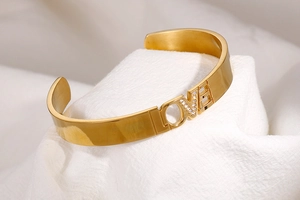 Detail of gold LOVE open bangle with sparkling cubic zirconia inlay on white silk