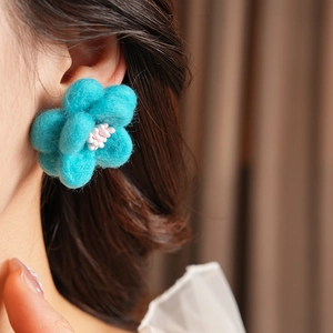 Détail des boucles d'oreilles fleur en feutre bleu avec perles roses portées par un modèle