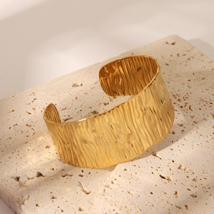 Gros plan détaillé d'un bracelet manchette doré large avec texture d'écorce sur pierre