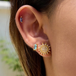 Macro shot of gold sun earrings with white diamonds and blue gemstones on ear