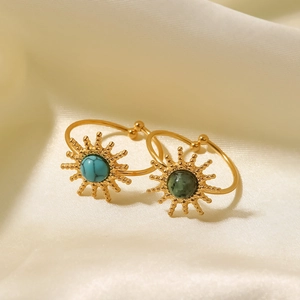 Detail of sun-shaped gold rings with turquoise stones on elegant beige silk fabric
