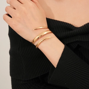 Dettaglio del bracciale rigido a spirale dorato minimalista sul polso della modella
