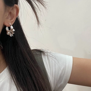 Detail view of a silver bow earring in a metallic finish worn by a model in profile