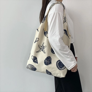 Detailed side view of beige canvas tote bag with ocean shell prints on model