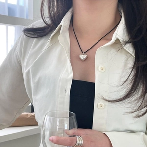 Close-up of minimalist silver heart pendant with black cord and tiered silver ring