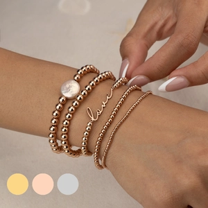 Close-up of bohemian layered 14K gold plated bracelets with pearl and love charm