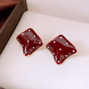 Macro view of dark red enamel rhombus earrings with white polka dots and gold trim