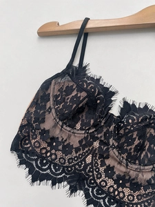 Detail shot of delicate black eyelash lace bra with nude mesh lining on wooden hanger