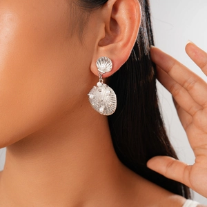 Detailed view of silver shell-shaped earrings with pearls worn by a fashion model