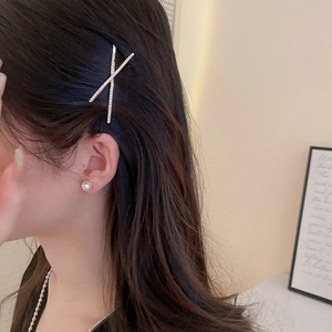 Detailed view of a sparkling X-shaped gold hair clip with crystal rhinestones on a model