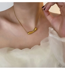 Close-up of a sleek gold teardrop pendant on a fine chain worn with an elegant white top