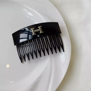 Detail view of a black resin hair comb featuring a gold H letter logo on a white plate