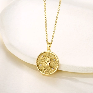 Golden coin necklace with engraved rose and zircon stones on a white ceramic plate
