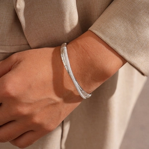 Close-up of a silver crossover bangle with zircon pave set on a beige suit sleeve