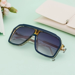 Square dark blue sunglasses with gradient lenses and cream leather case on green surface
