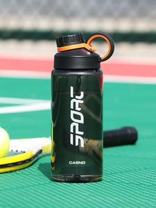 Close-up of green sports water bottle with black lid and orange handle on a tennis court