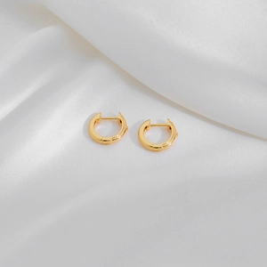 Detail of gold huggie hoop earrings resting on white silk fabric with elegant lighting