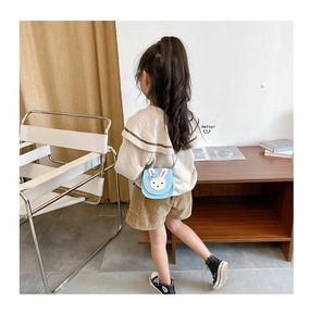 Close-up of a blue bunny crossbody bag with embroidery worn by a child in a home setting