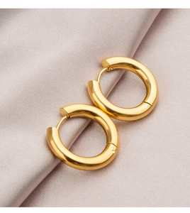Macro shot of gold titanium hoop earrings on elegant light purple textured silk background