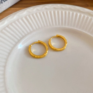 Detailed view of golden hammered hoop earrings on a white ceramic dish and wooden table