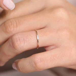 Macro shot of a slim 18K gold ring with three clear zircons on a model's finger