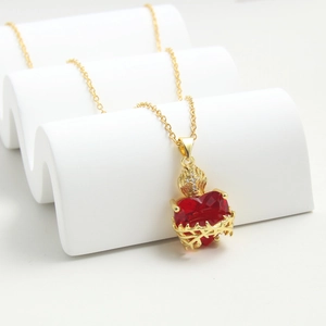 Golden cross pendant necklace with a red heart zircon stone on a white display stand
