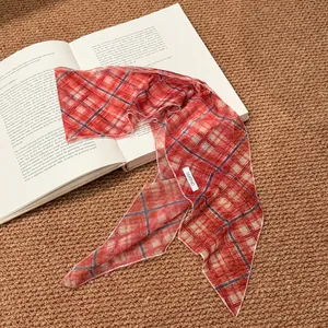 Close-up detail of a vintage red plaid fabric scarf necklace placed on an open book
