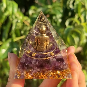 Macro shot of purple amethyst crystal resin pyramid with golden Buddha figure detail