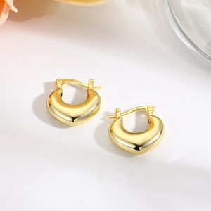 Macro view of gold-plated hollow heart earrings with smooth polished finish on white surface