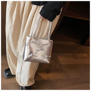 Silver metallic square handbag with bow detail and chain strap worn by a model