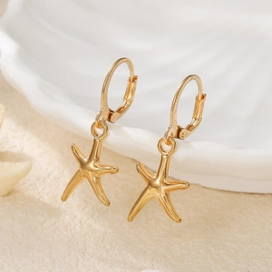 Close-up of gold starfish drop earrings hanging on a white shell-shaped decorative bowl
