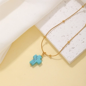 Detail of a gold ball chain necklace with a blue turquoise cross pendant on white silk