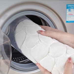 Close-up of flexible 3D pebble textured bathroom mat being placed in a washing machine