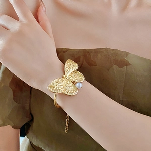 Detailed macro of gold butterfly bracelet with relief texture and a white pearl accent