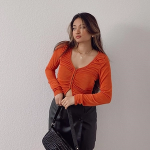 Détail d'un cardigan plissé orange avec une mini-jupe en cuir noir et des accessoires chics