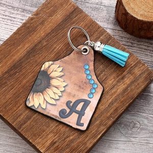 Western style leather sunflower keychain with blue tassel and letter A on wood background