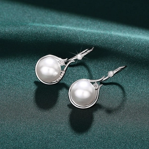Close-up of elegant silver pearl earrings with small diamonds on green silk background