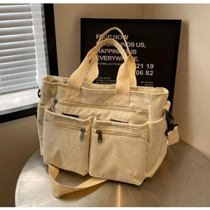 Detail of off-white corduroy tote bag showing front zipper pocket and dual handles