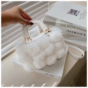 Detail of white faux fur handbag with leather handle and gold metal ring on white books