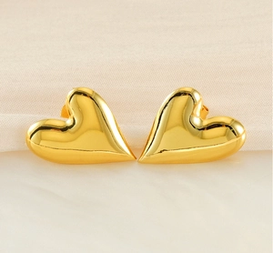 Detailed close-up of chunky gold 18K plated heart stud earrings on silk fabric